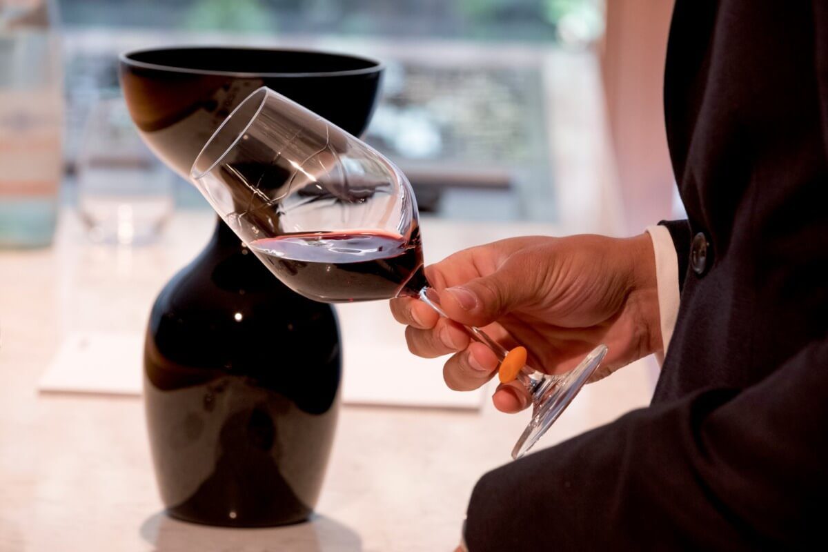 Detail shot of hand holding glass of red wine tilted at an angle