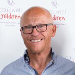 Portrait of british entrepreneur John Caudwell in front of Caudwell Children sign