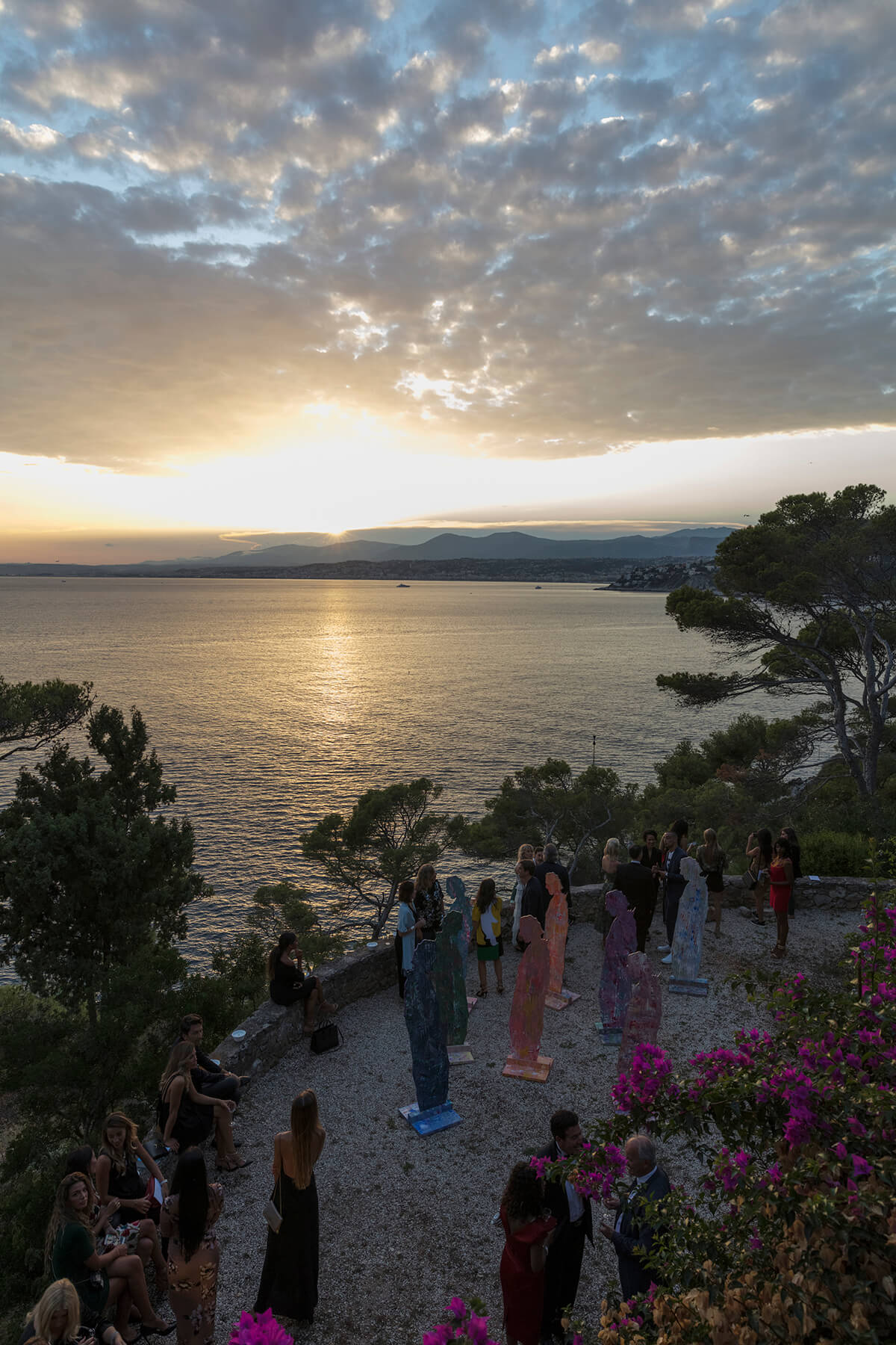 Party on the edge of the sea as the sun is setting people gather around colourful sculptures