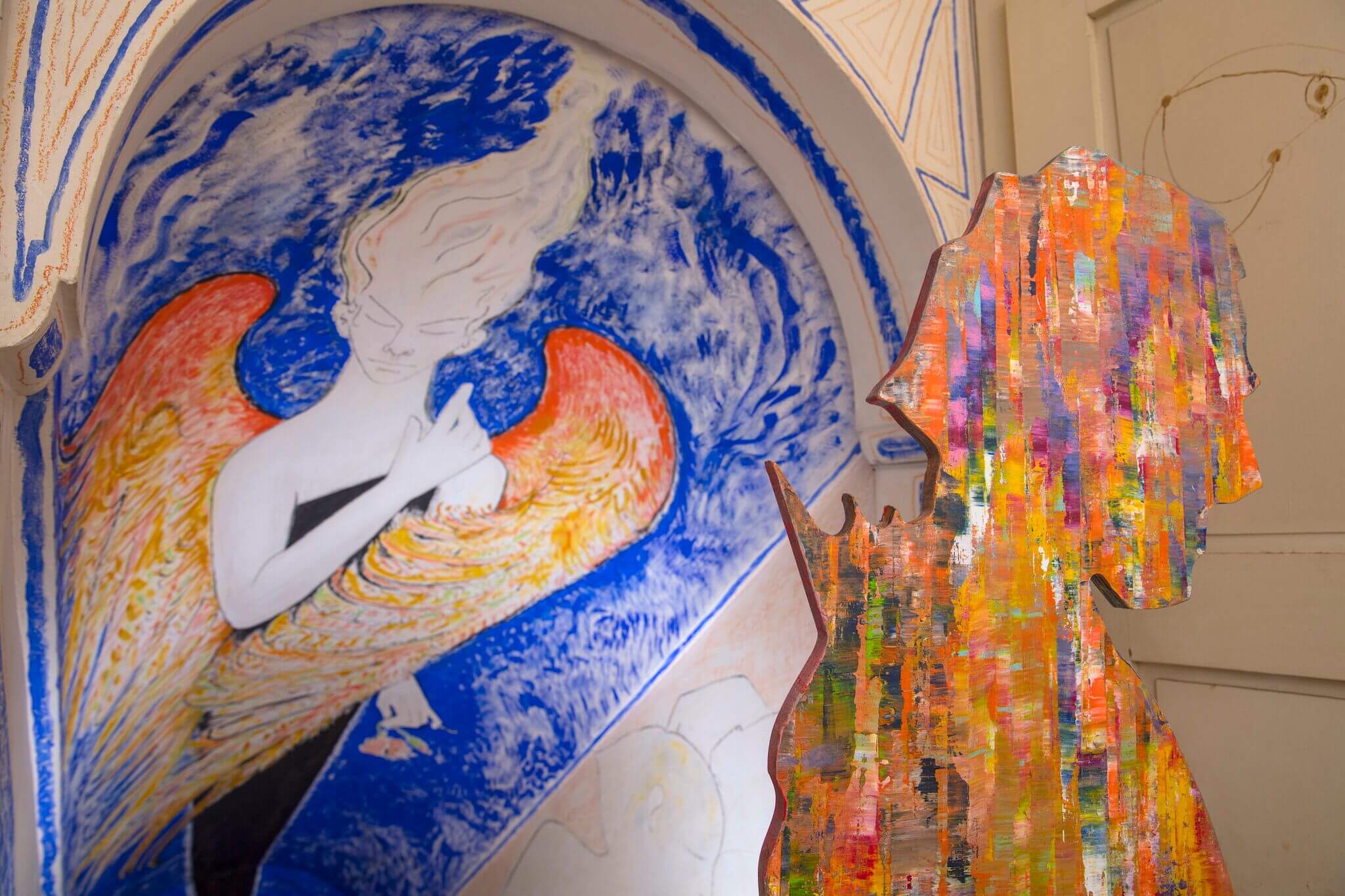 Sculpture of a man in front of colourful mural depicting a mystical figure