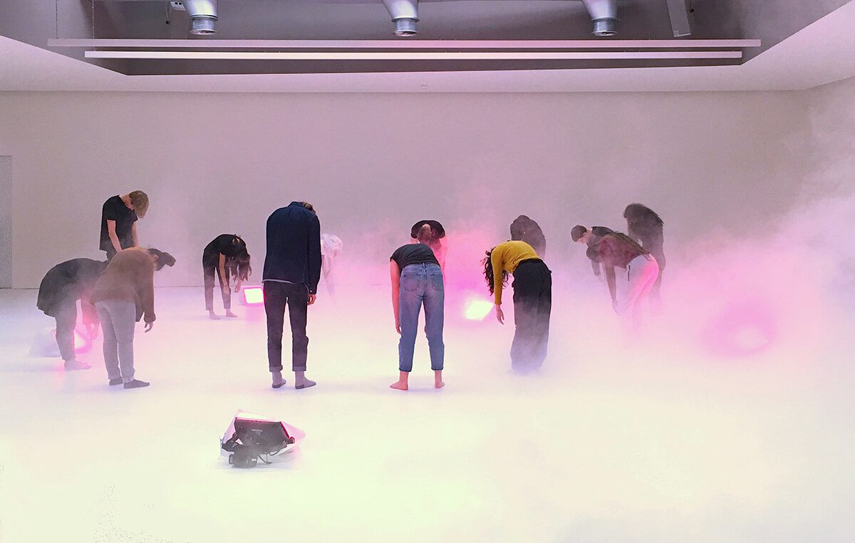 Performance art scene of people hanging over surrounded by mist and pink lights