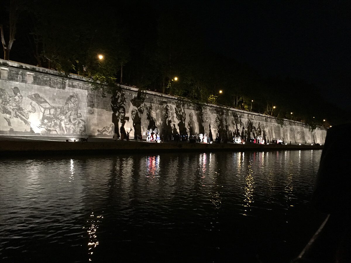 Public art mural lit up on a wall along a rive