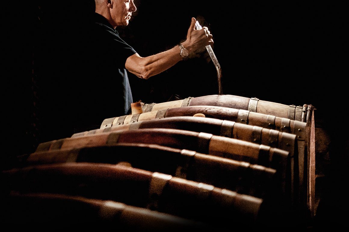 Man testing wine from a line of oak barrels