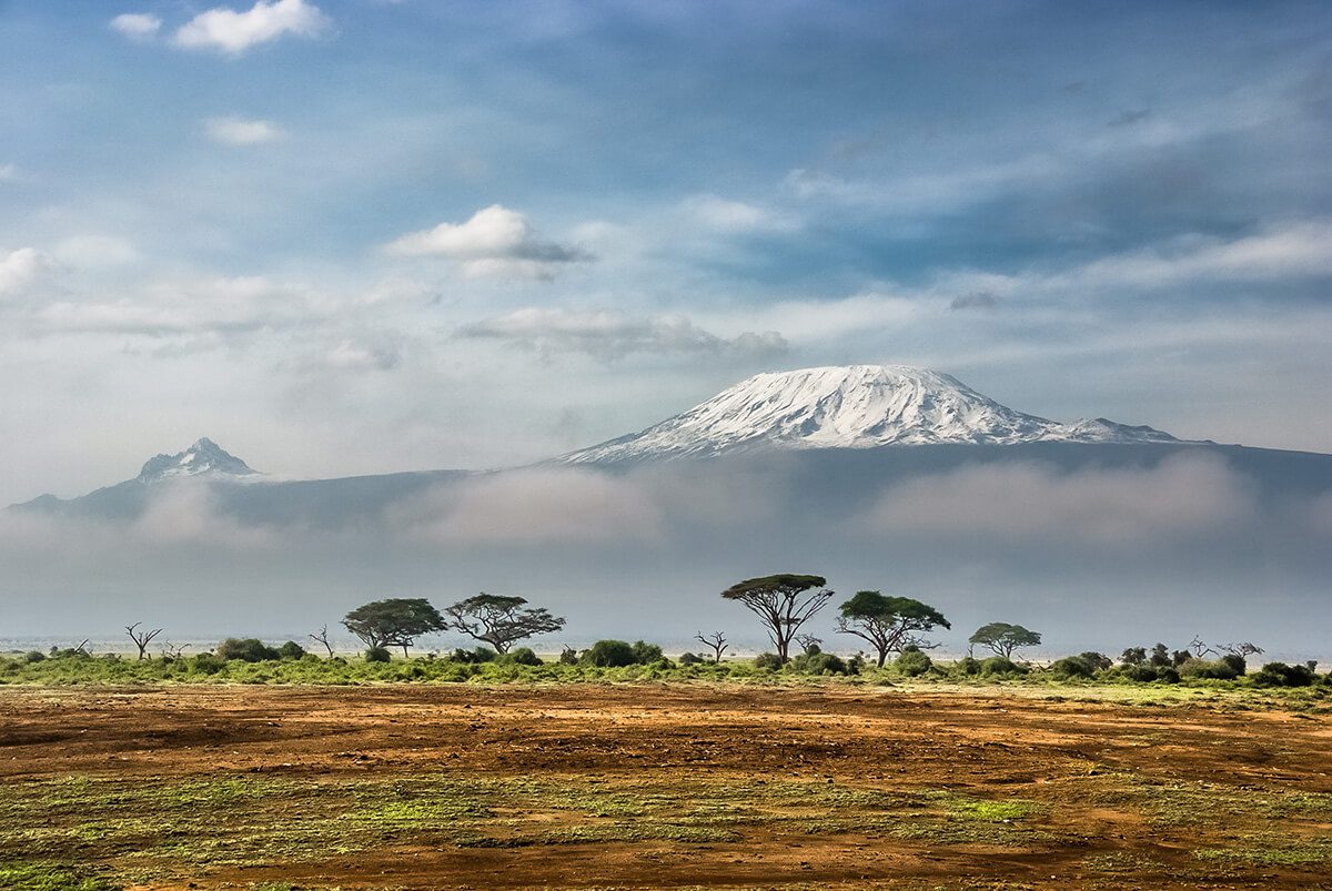 The snow-capped peak of Mount Kilimanjaro covered partially by clouds with plains in front