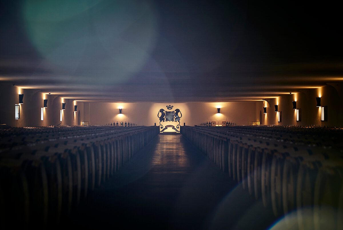 A large wine cellar with rows of barrels and a crested back wall