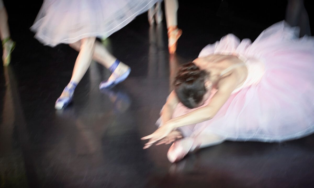 Ballet dancers in motion with one dancer stretching on the ground