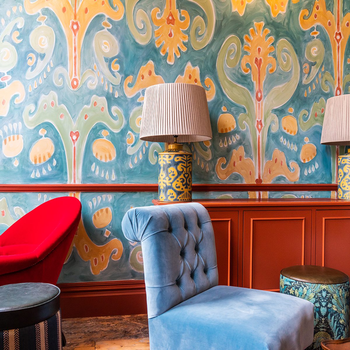 Detail interior shot of an elaborately patterned wall with a lamp and velvet chair