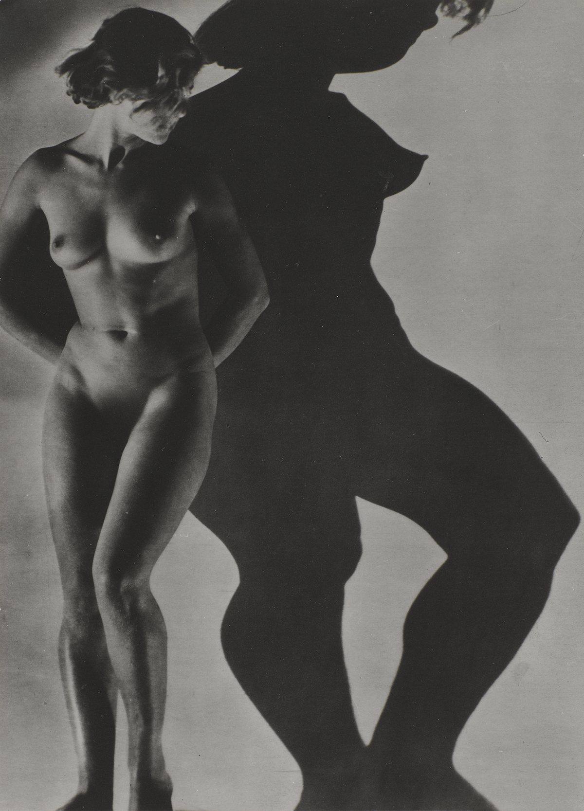Naked woman photographed against a wall with her shadow