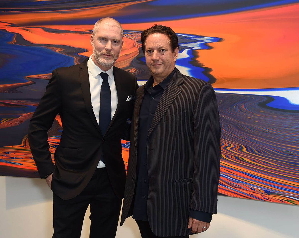 Two men in suits stand in front of psychedelic painting 
