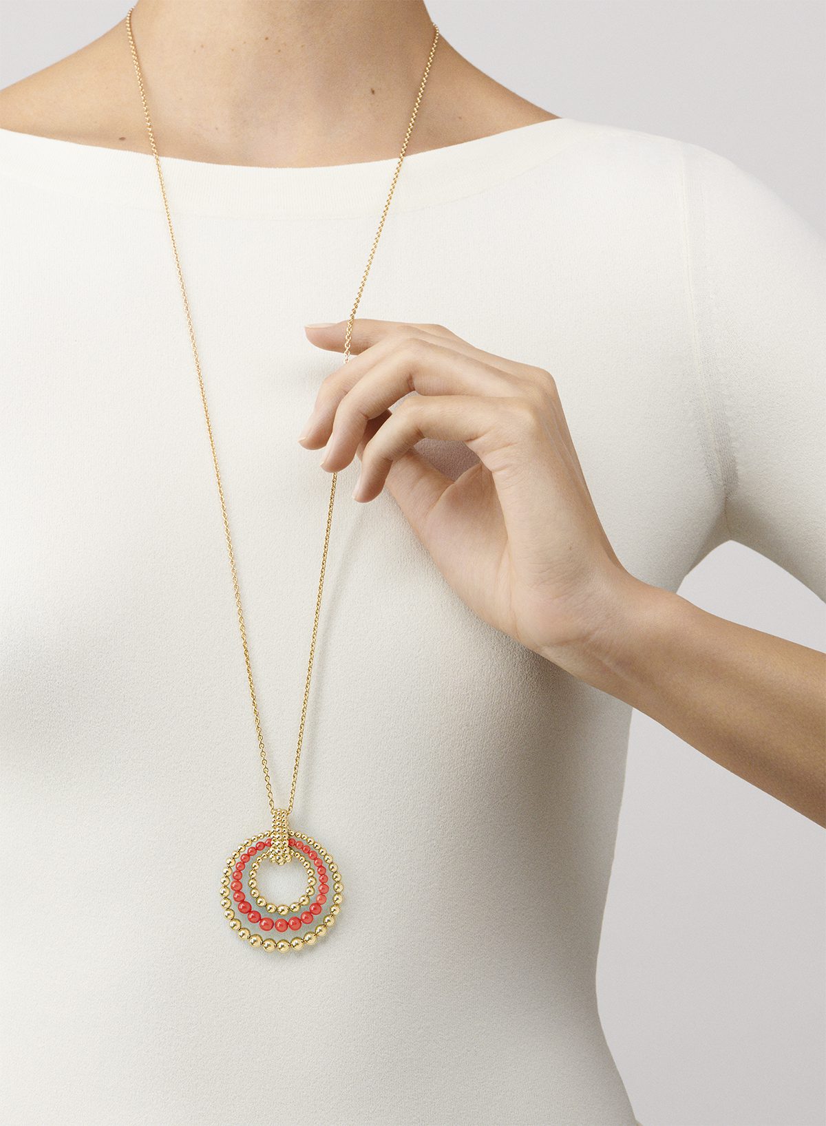 promotional image of a woman's torso in a white top wearing a long chain necklace with a beaded circle pendant