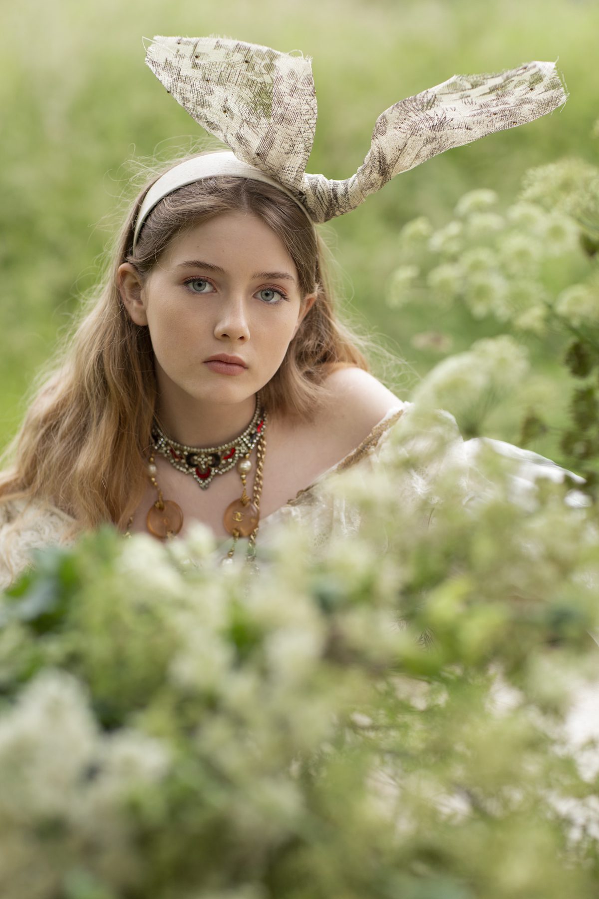 Young female model crouched in the long grass wearing a headpiece