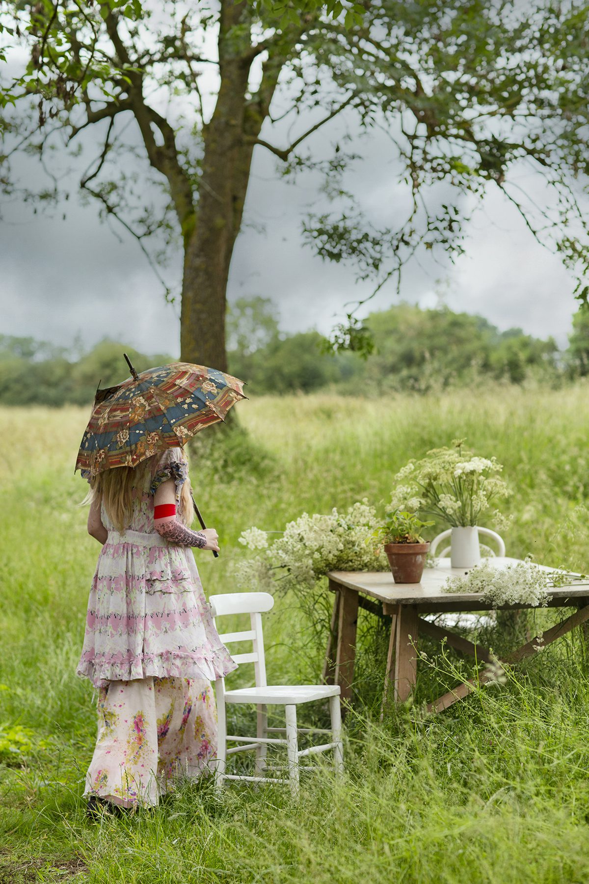 Woman walking through field with a parasol and wearing long dress