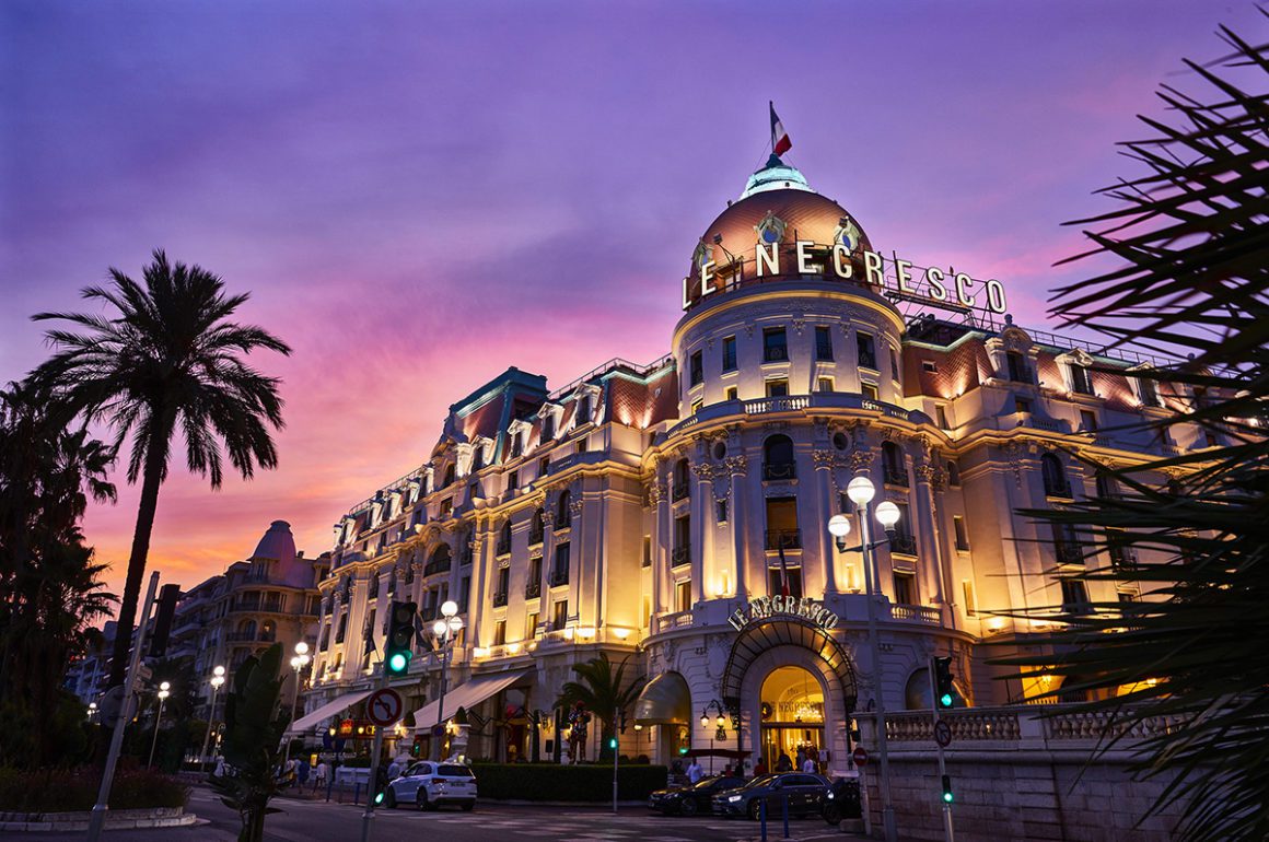Facade of a hotel at night lit with a purple sunset behind
