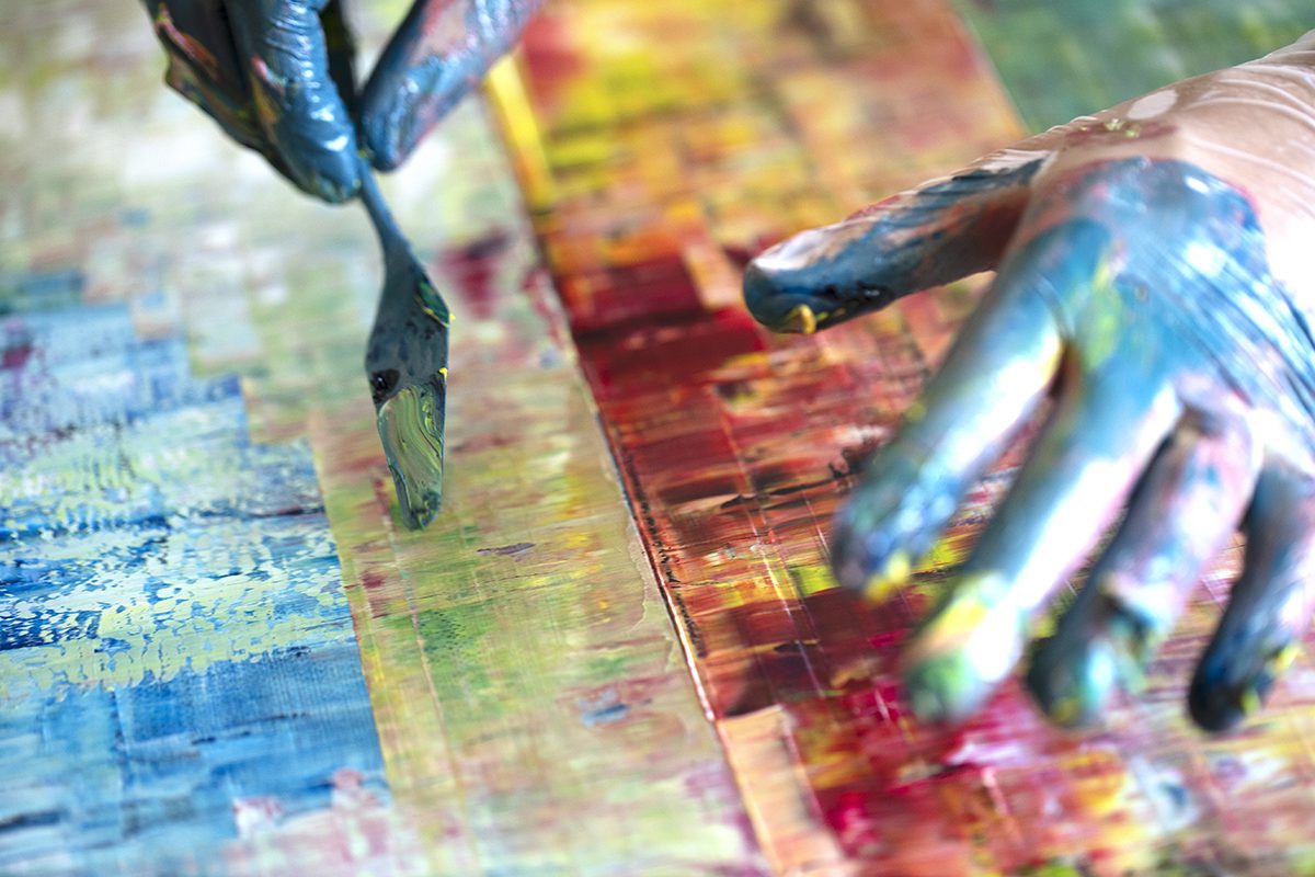 Painter's hands using a scraper to shave paint on a canvas