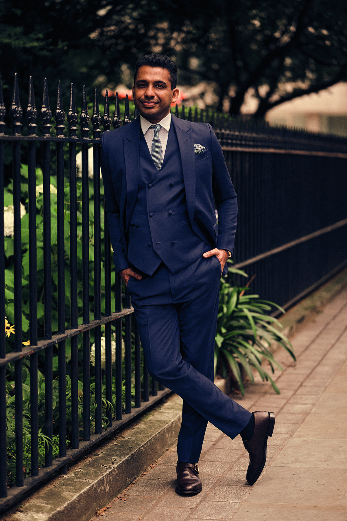 man leaning against fence wearing a suit