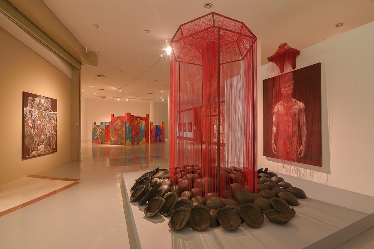 red string dripping from the wall and a man in a painting behind it in an art gallery