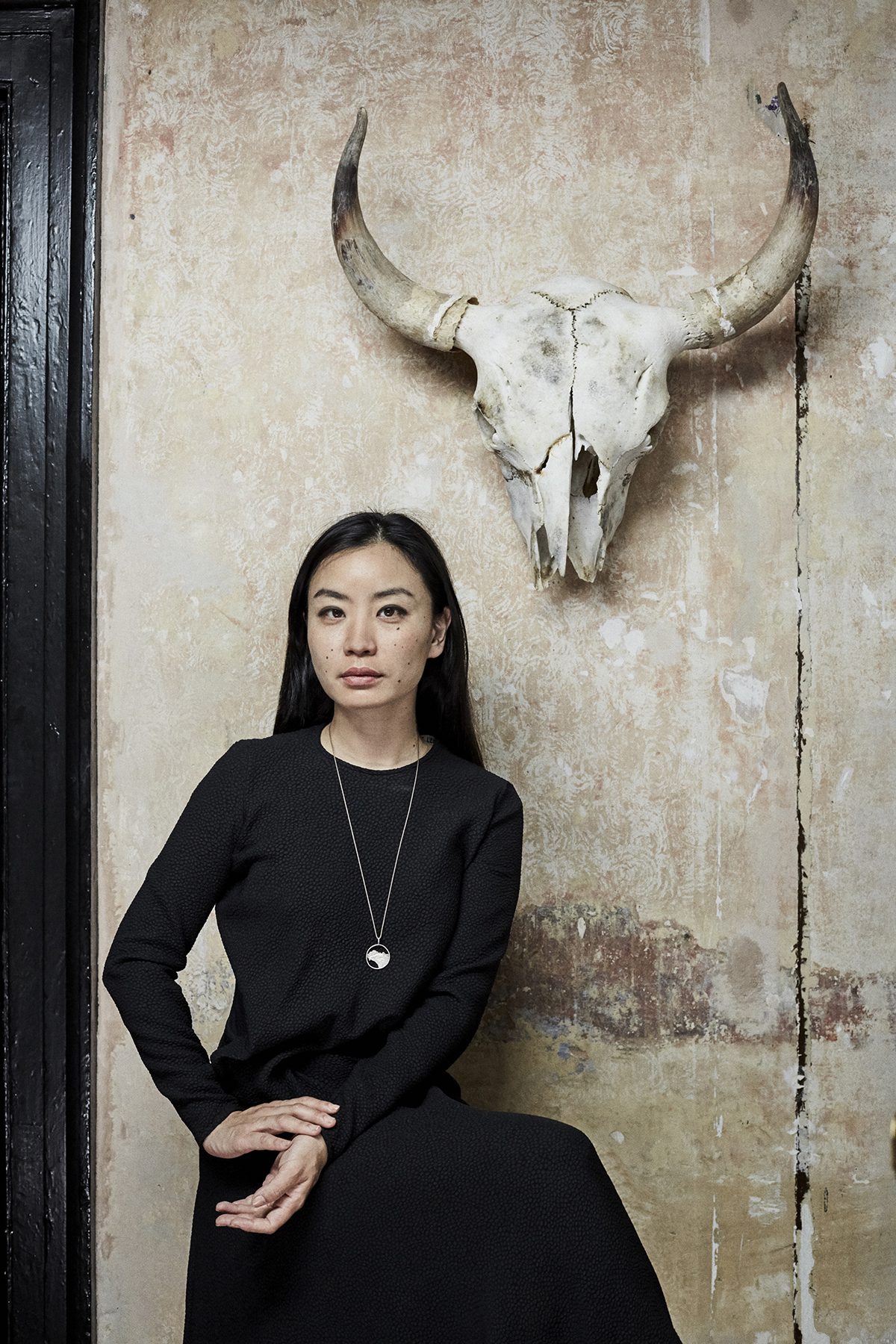 A woman standing in a black dress underneath the skull of a bull