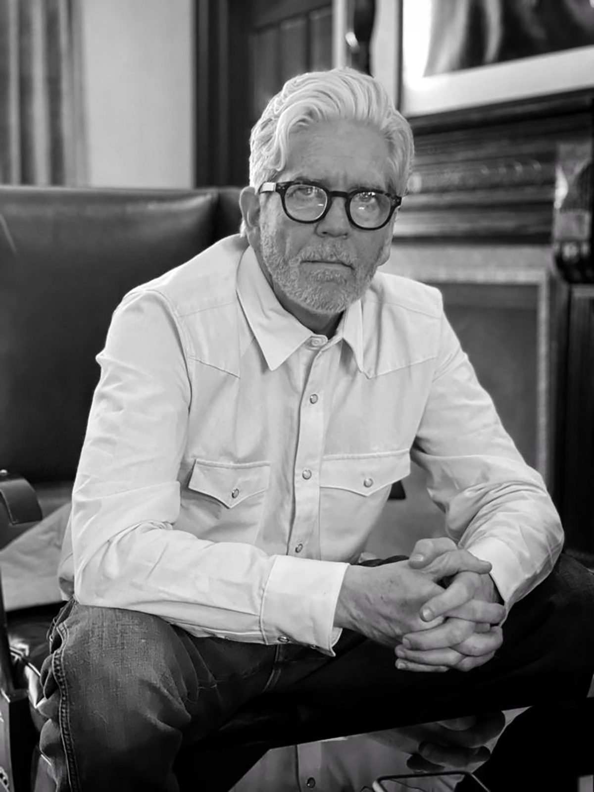 A man wearing a white shirt with his hands together sitting on a chair