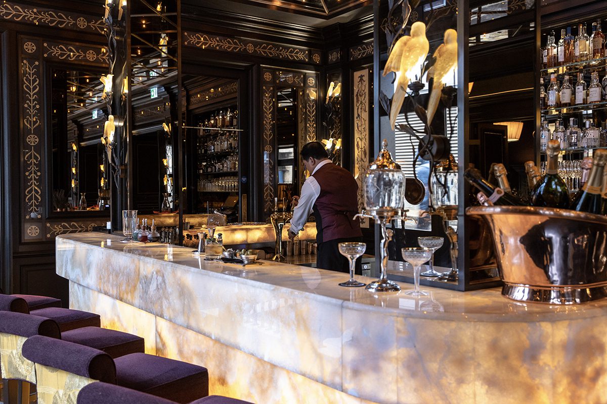 A marble bar with purple seats and a man serving behind the bar 