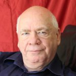 A bald man in a black shirt with a red background