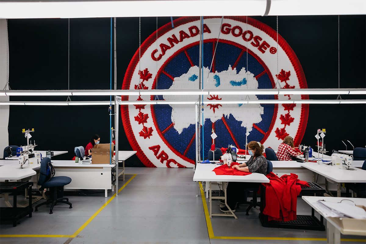 Canada Goose logo on a wall in a factory where a woman is sewing with a machine