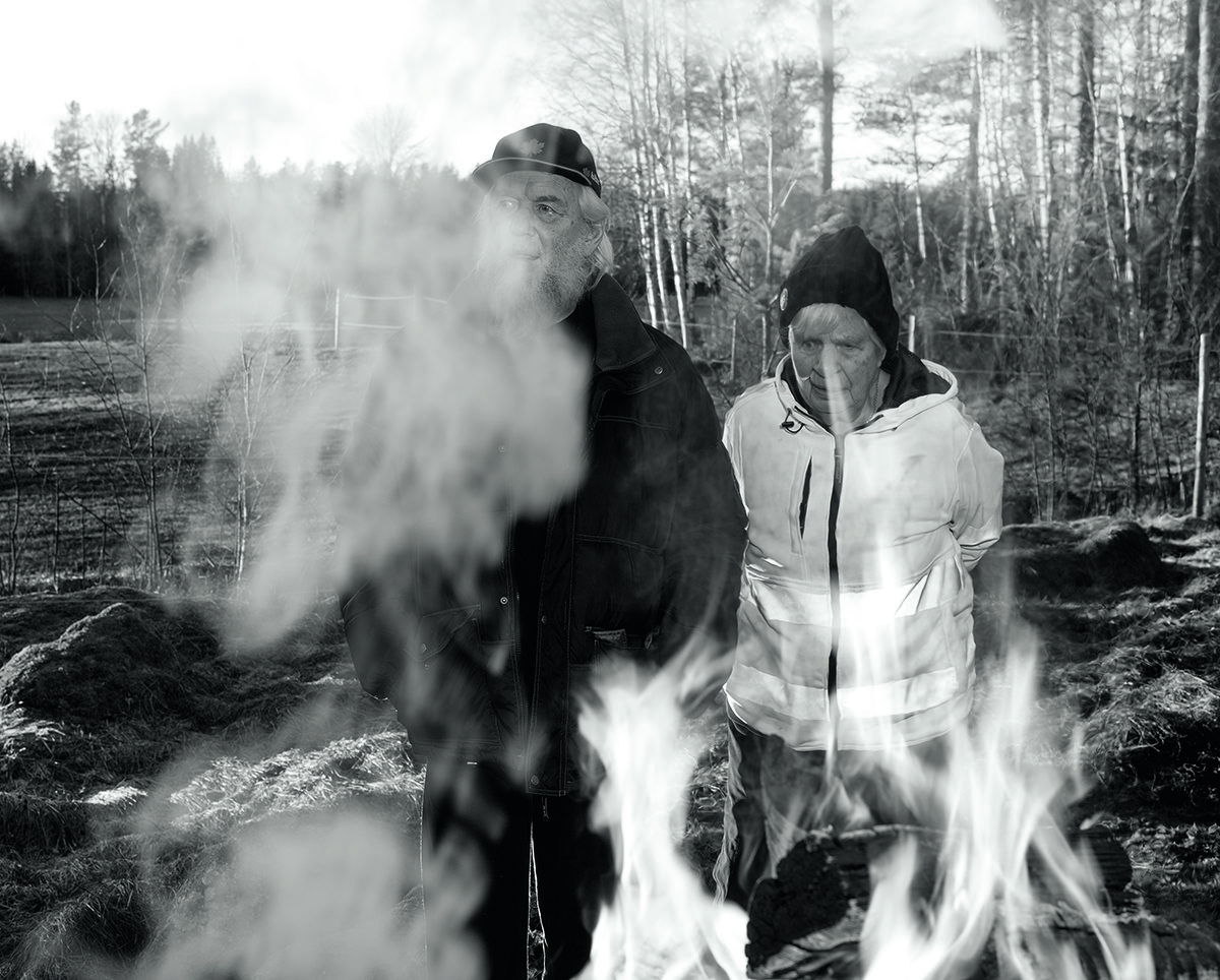 black and white image of a man and woman standing over a barbecue