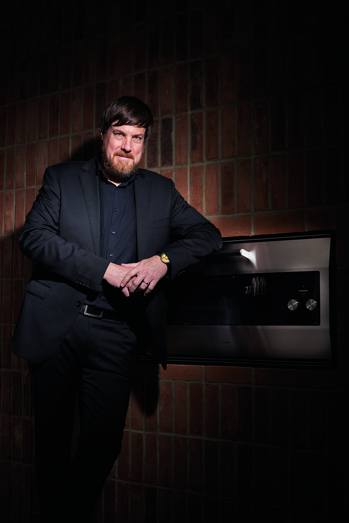 A man in a black suit sitting in a brown room 