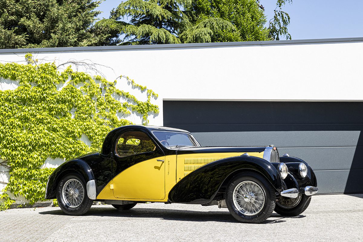 black and yellow classic car in front of a garage 