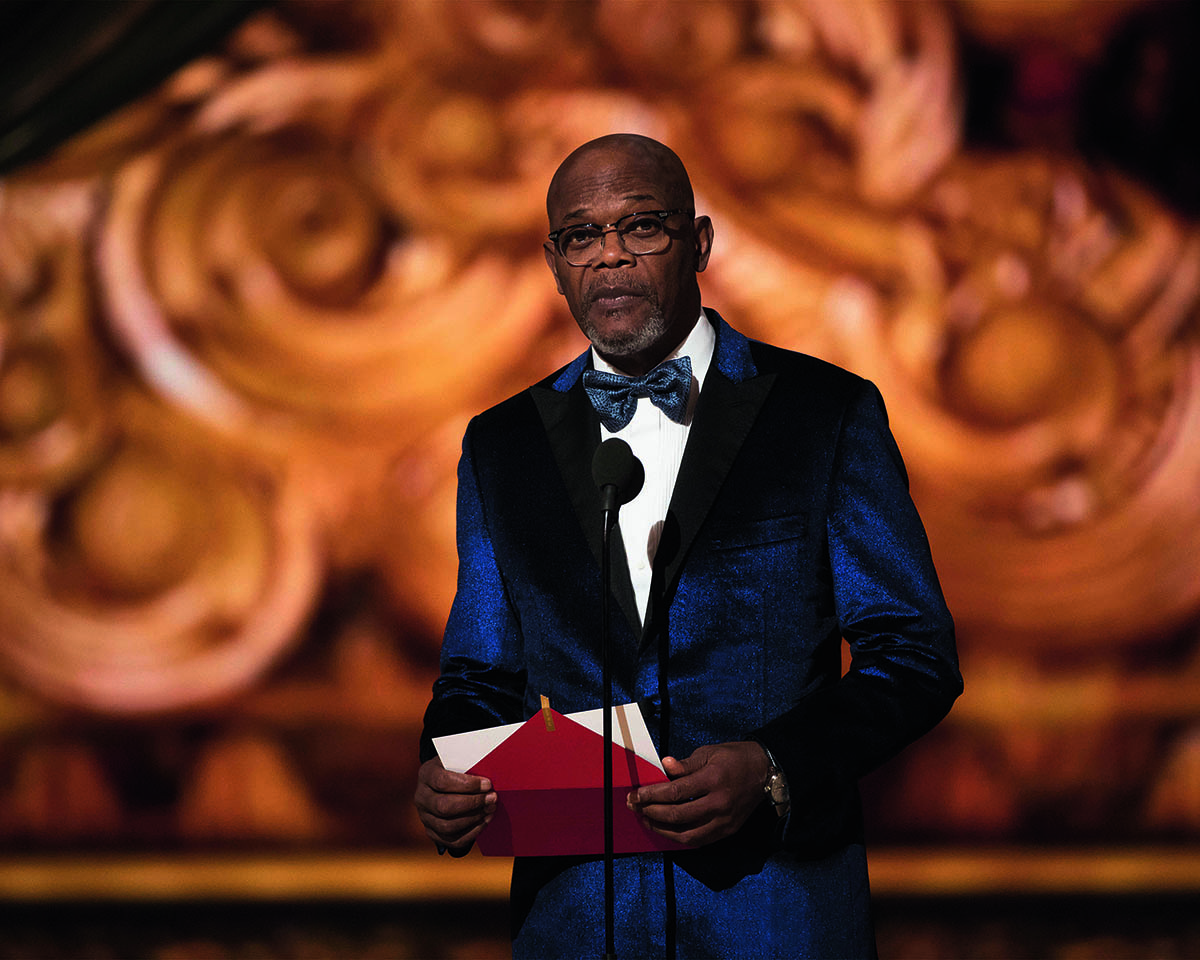 A man wearing a navy blue suit presenting an award