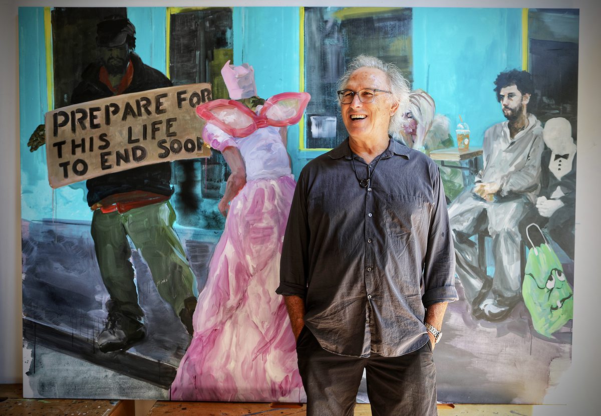 A man wearing a grey and black jeans and shirt standing in front of a painting 