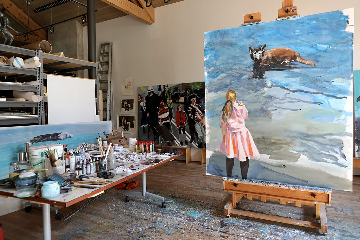 A painting of a girl in a pink dress and a dog upright in a studio