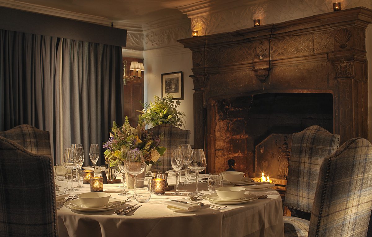 A dinner table set by a fire with tartan chairs