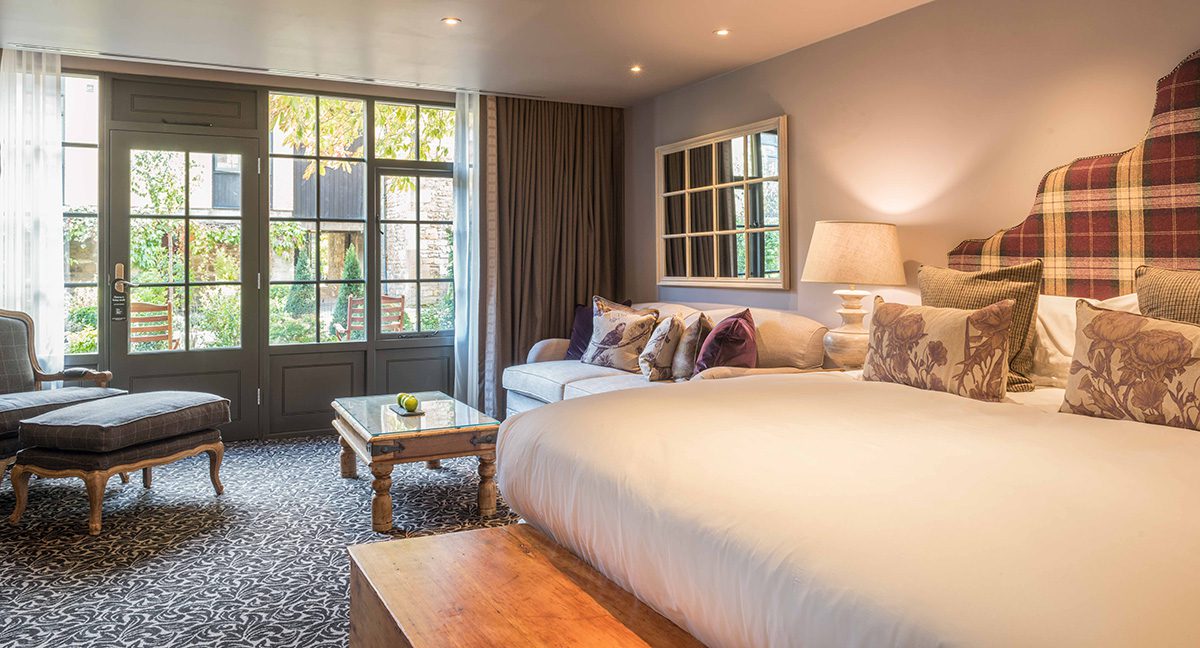 A room with a white bed and sofa leading to a courtyard
