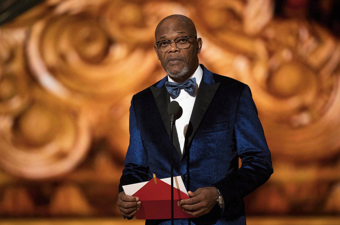 A man wearing a navy blue suit presenting an award