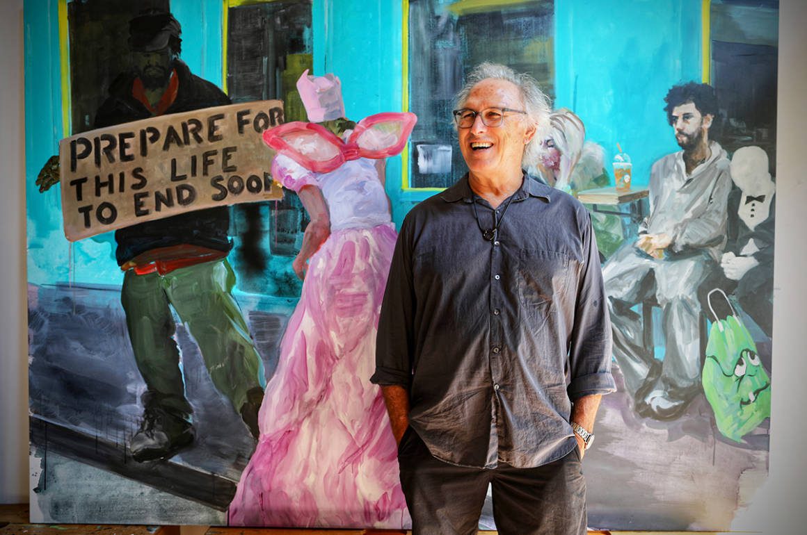 A man wearing a grey and black jeans and shirt standing in front of a painting