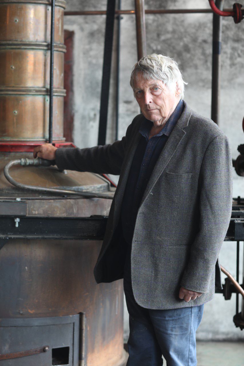 A man in a grey jacket and black shirt standing next to a barrel