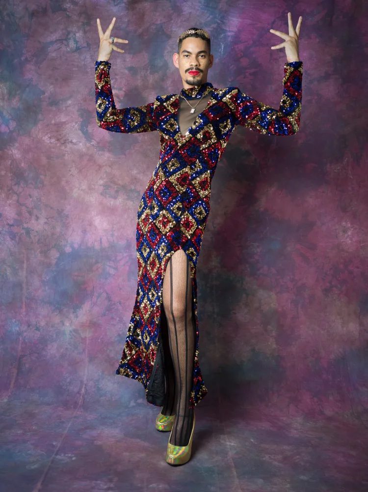 A man in tights and a dress standing in front of a purple wall