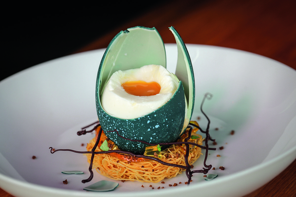 An egg yolk with a blue shell on crispy noodles and brown sticks on a plate