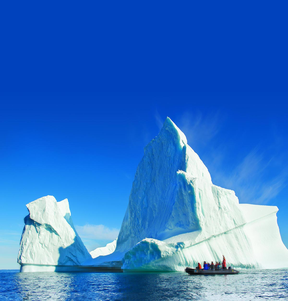 An iceberg in the sea with people looking at it from a speed boat