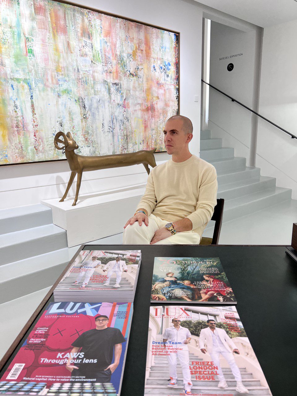 A man sitting on a chair next to a table with LUX magazines on it