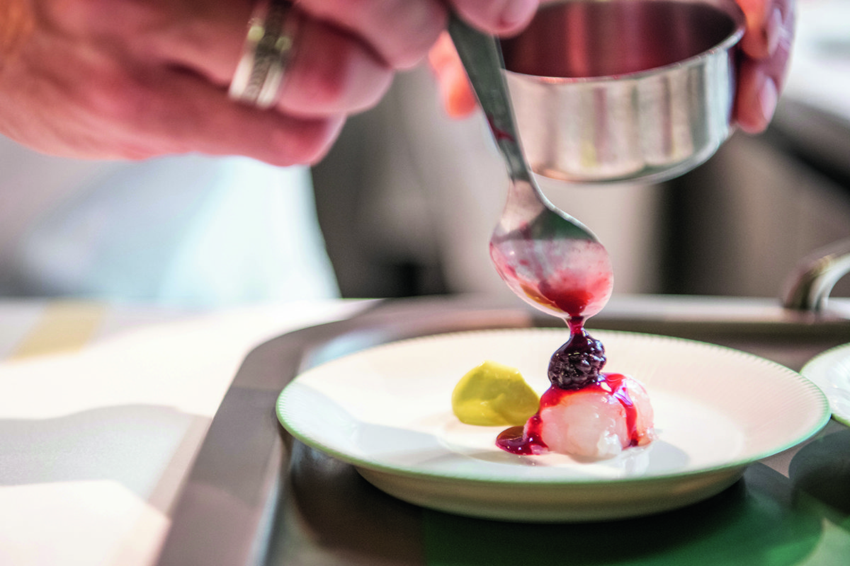 someone using a spoon to drizzle raspberry coulis on a dessert
