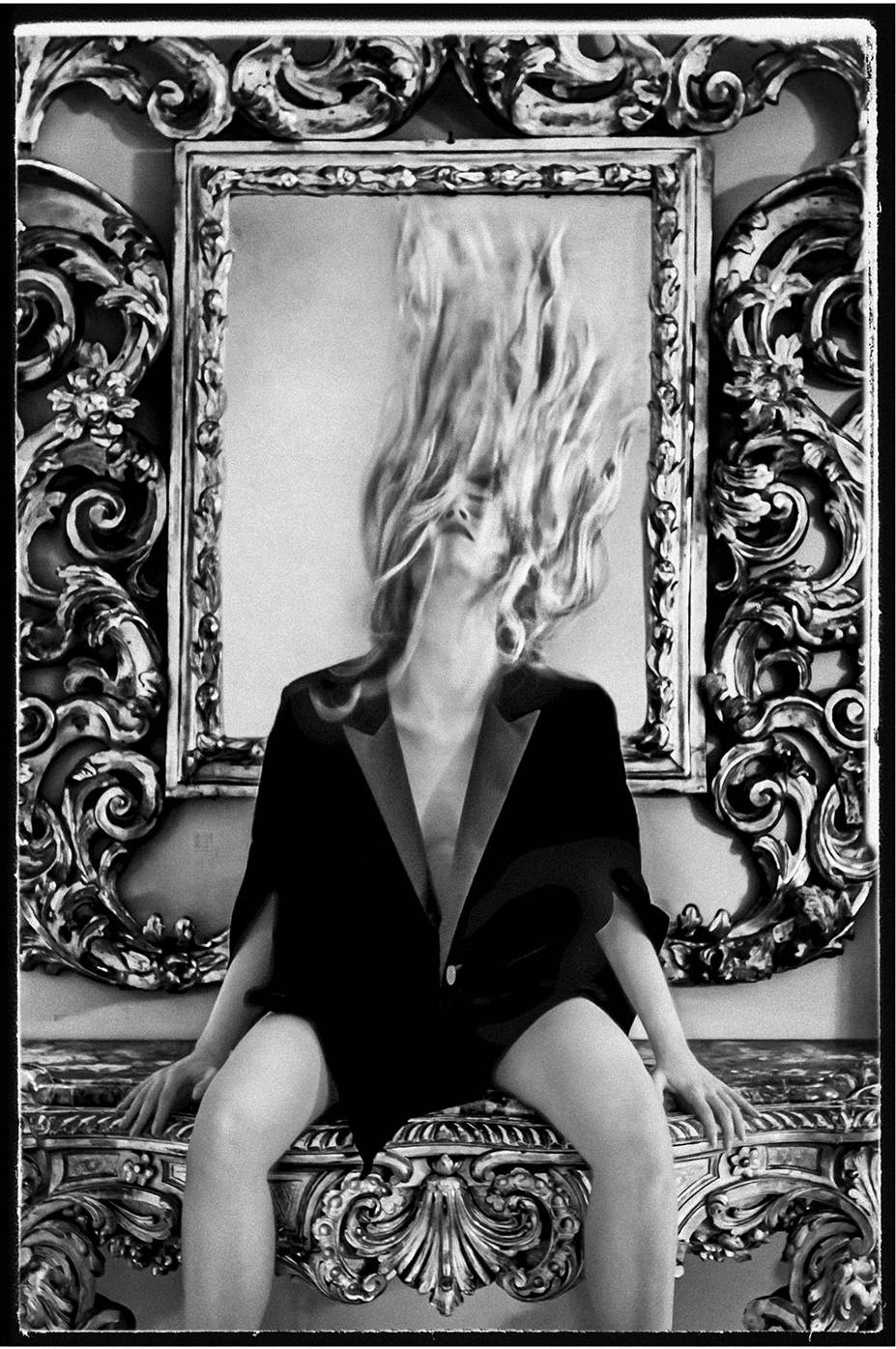 A woman sitting on a sofa wearing a black blazer flipping her back