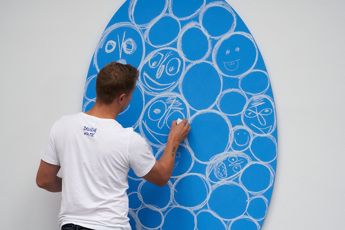 A man in white t shirt drawing with chalk on a blue panel