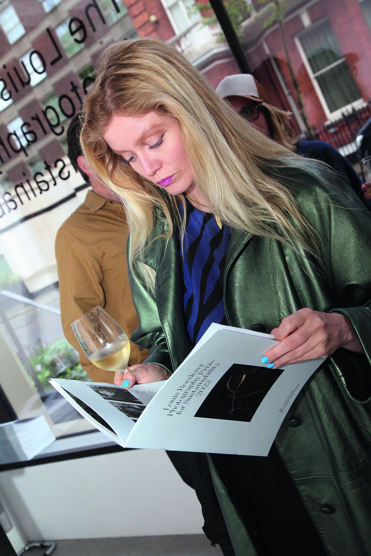 A blonde woman wearing a green coat reading a catalogue