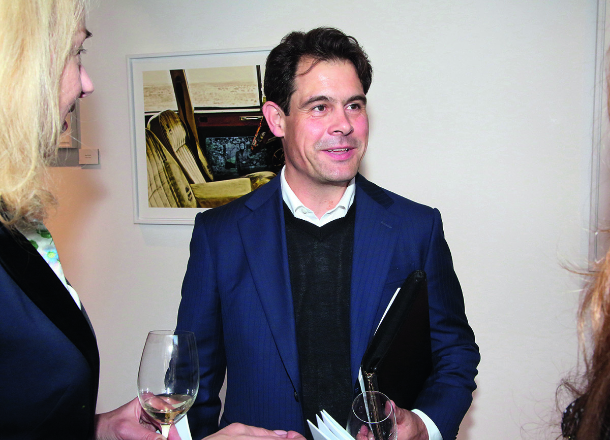A man wearing a black jumper, white shirt and blue blazer