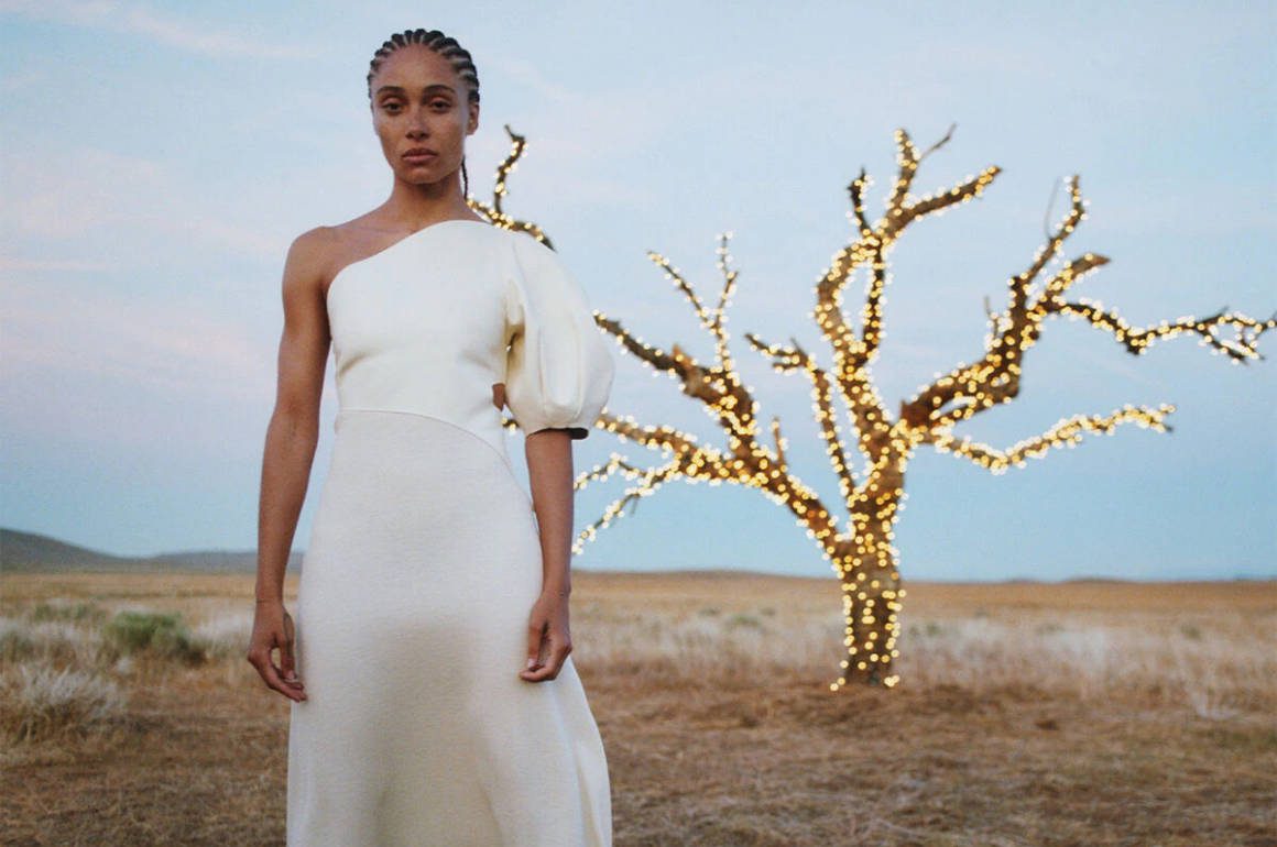 A woman wearing a white dress standing next to a lit up tree in a desert