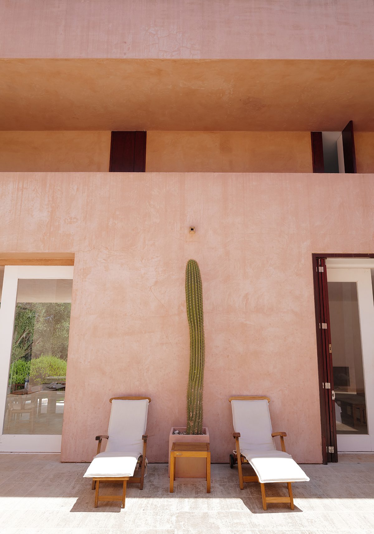 Two deckchairs in front of a pink wall and a cactus between them