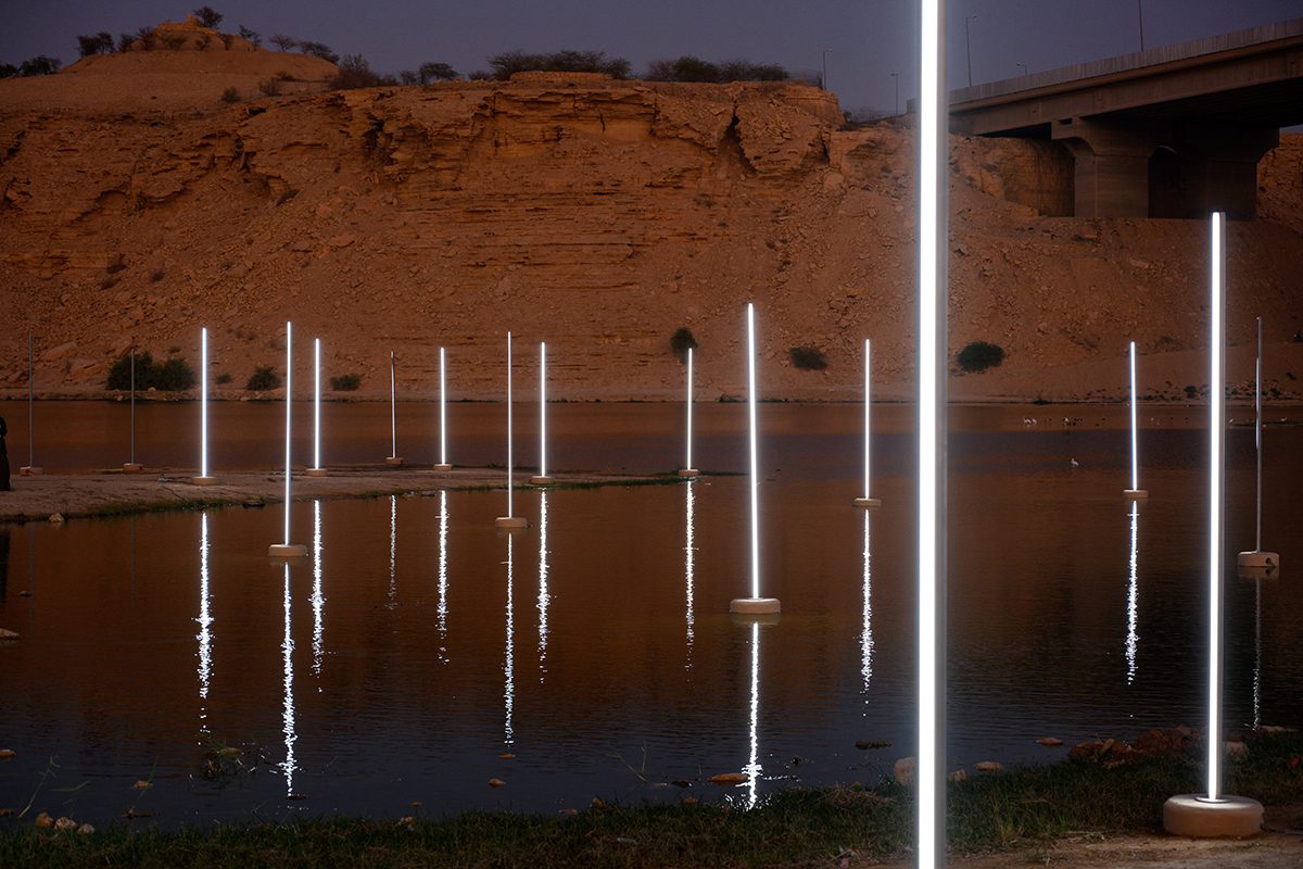 lit up poles on a river by sand dunes