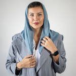 A woman wearing a blue headscarf and grey blazer with a black watch