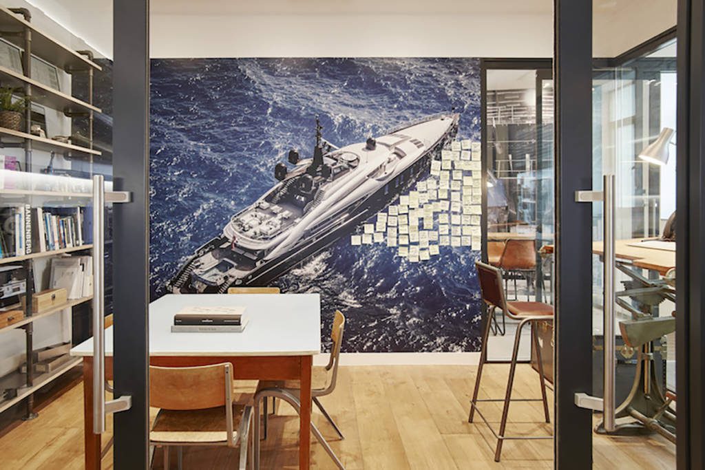A picture of a boat on a wall with sticky notes on it in an office with a brown chair and white table